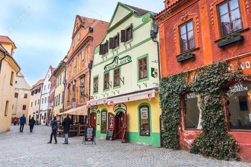 Una strada acciottolata fiancheggiata da edifici colorati, tra cui un edificio verde e giallo con un cartello che recita 'Wiener Museum'. 1