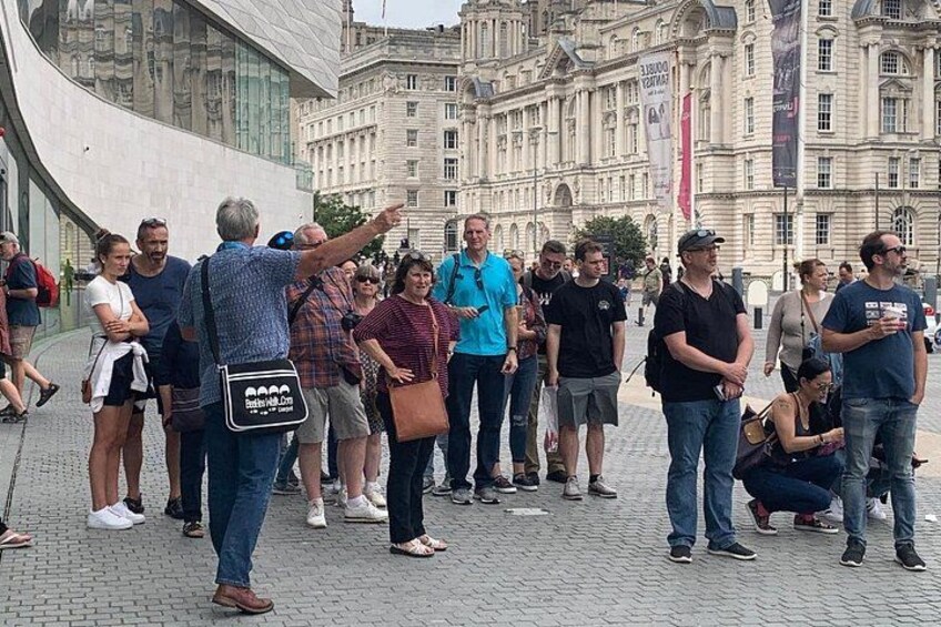 Un gruppo di persone riunite in una piazza cittadina, con edifici storici sullo sfondo. 5