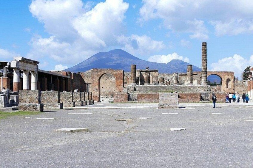 Ancient ruins with columns and arches, a mountain in the background, and tourists in the foreground. 1