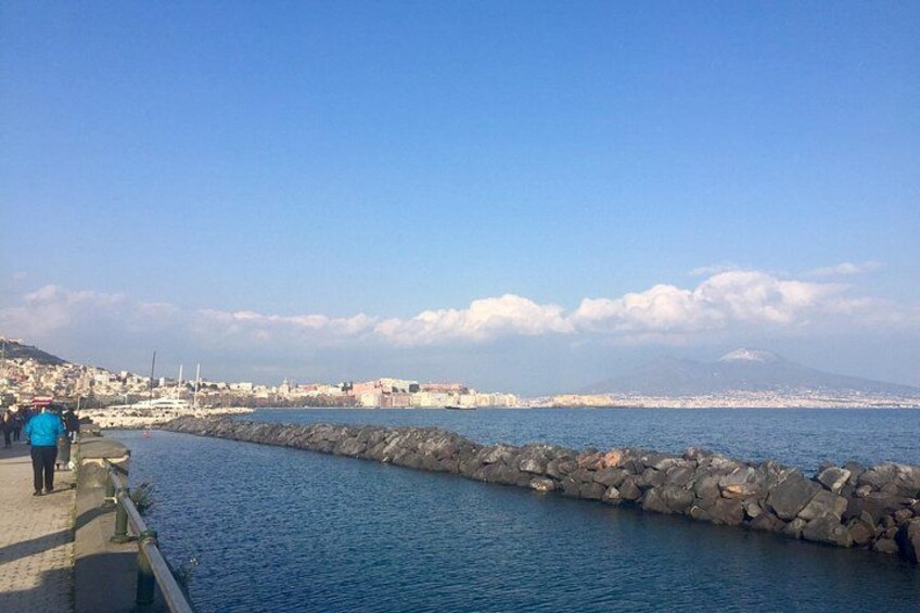 A coastal cityscape with a rocky breakwater, a clear blue sky, and distant mountains. 2