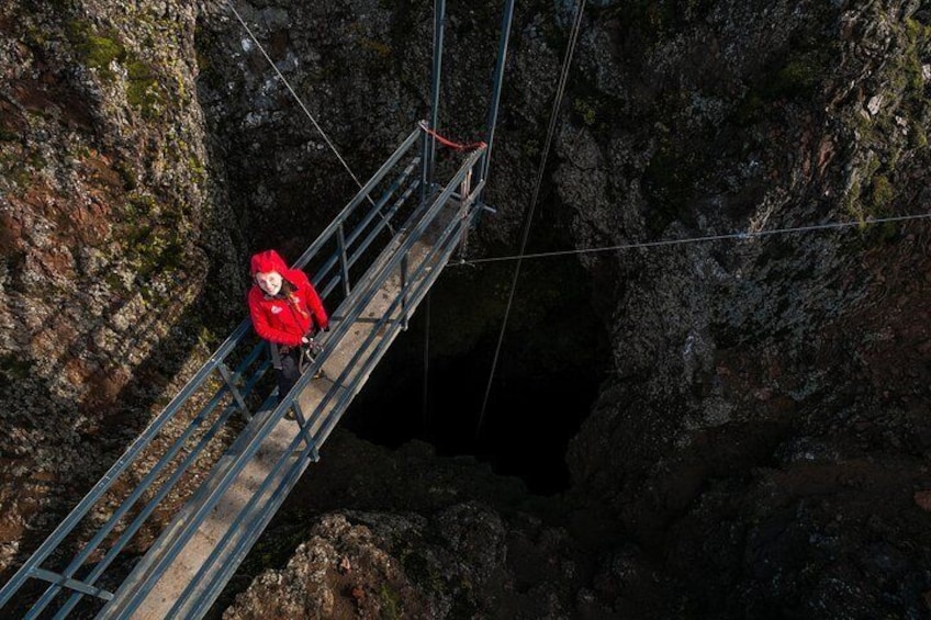 Eine Person in einer roten Jacke geht auf einer Metallbrücke über einer tiefen Schlucht. 4