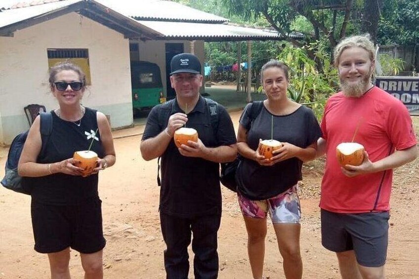 Four people holding coconuts in an outdoor setting with a building in the background. 3