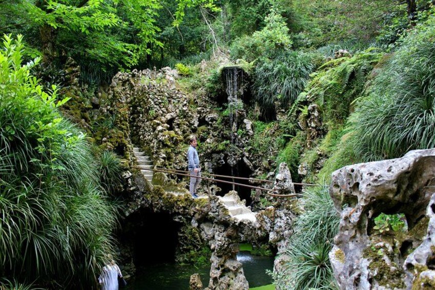 A person walking on a rope bridge over a rocky water body surrounded by lush greenery. 2