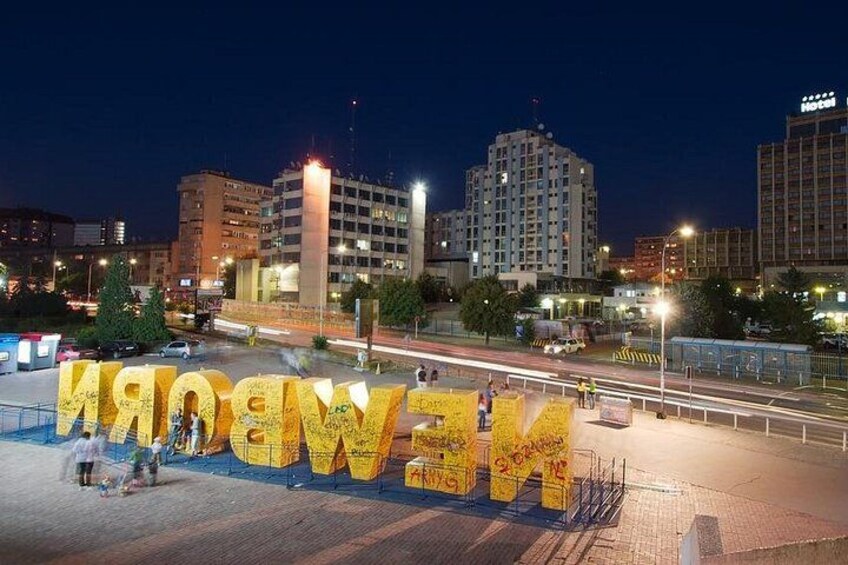 A nighttime cityscape with illuminated buildings and a large illuminated sign spelling 'NEWBORN.' 3