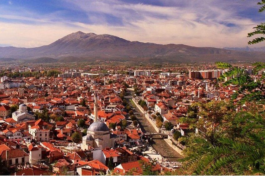 A cityscape with a prominent mountain in the background, a central road, and numerous buildings with red roofs. 2