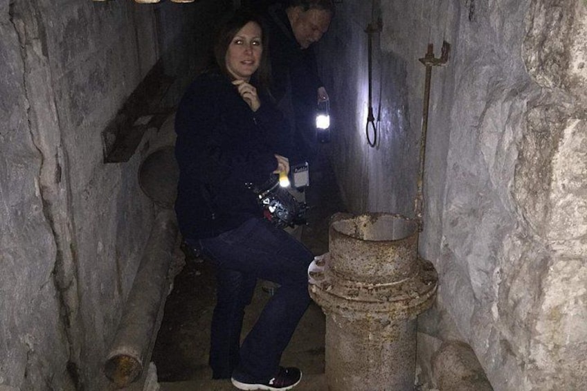 Eine Person in einem schmalen Steinkorridor mit einem Metallkübel und einer Taschenlampe. 2