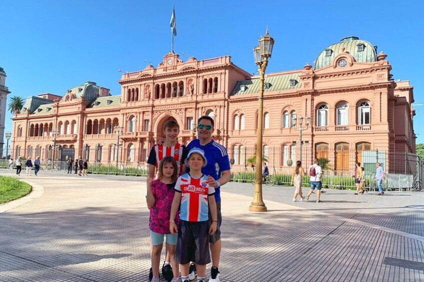 A family in front of a large pink building with a dome and arched windows. 2