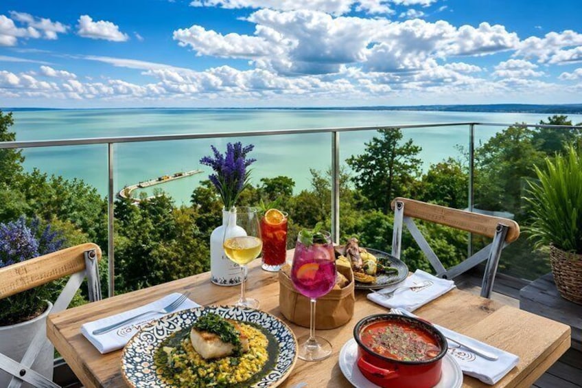 A table with food and drinks on a balcony overlooking a body of water. 2