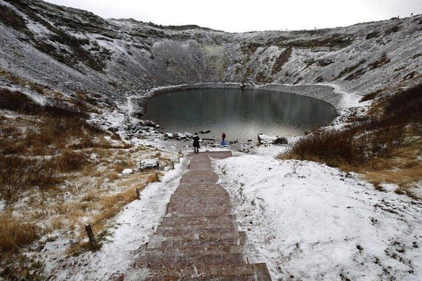Un paisaje nevado con un estanque circular, un camino de piedra que lo lleva hasta allí y una persona de pie junto al estanque. 2