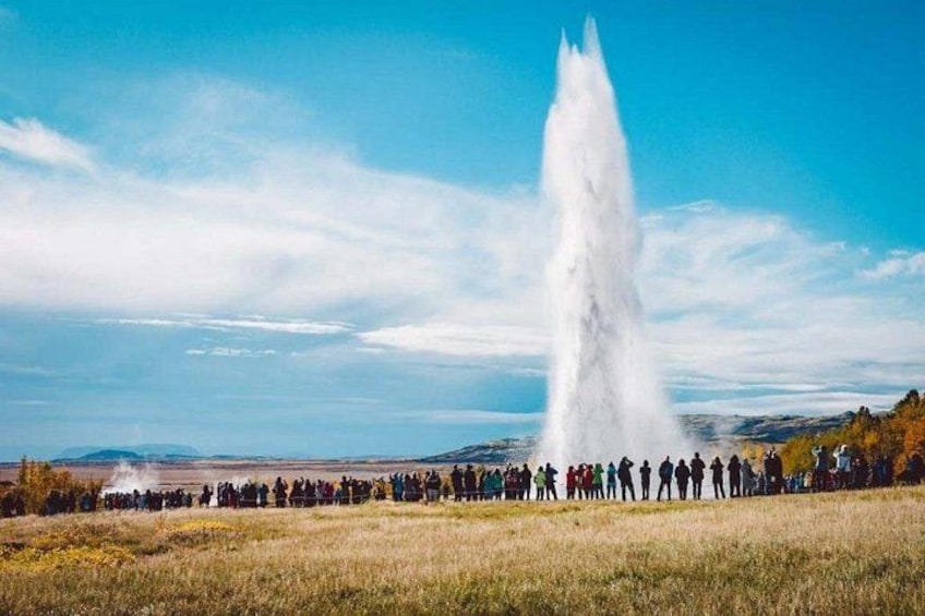 Una multitud se reúne alrededor de una alta fuente de agua en un campo cubierto de césped, bajo un cielo despejado. 5