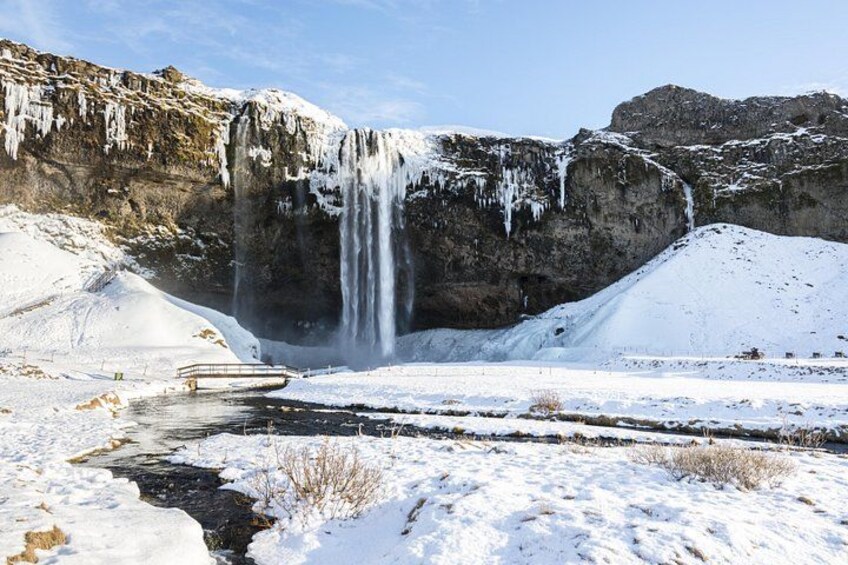 A snowy landscape with a waterfall, a bridge, and a river. 1