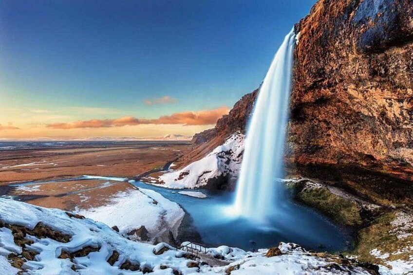 A waterfall cascading down a rocky cliff into a snow-covered valley. 4