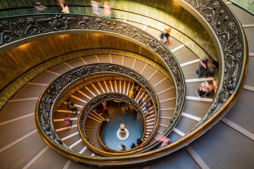 A grand spiral staircase with ornate metal railings and a central fountain. 2