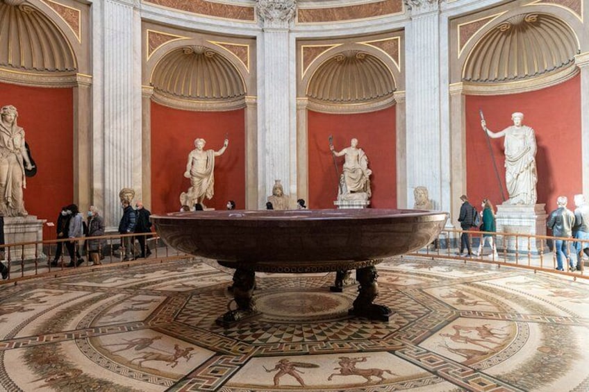 A museum interior with classical statues, a large bathtub, and intricate floor designs. 1