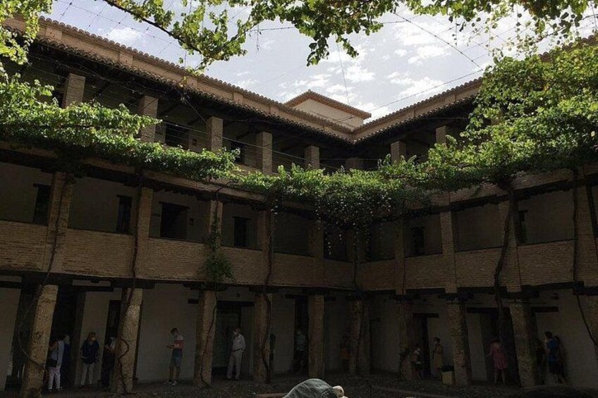 A courtyard with brick buildings, vines, and people standing in doorways. 3