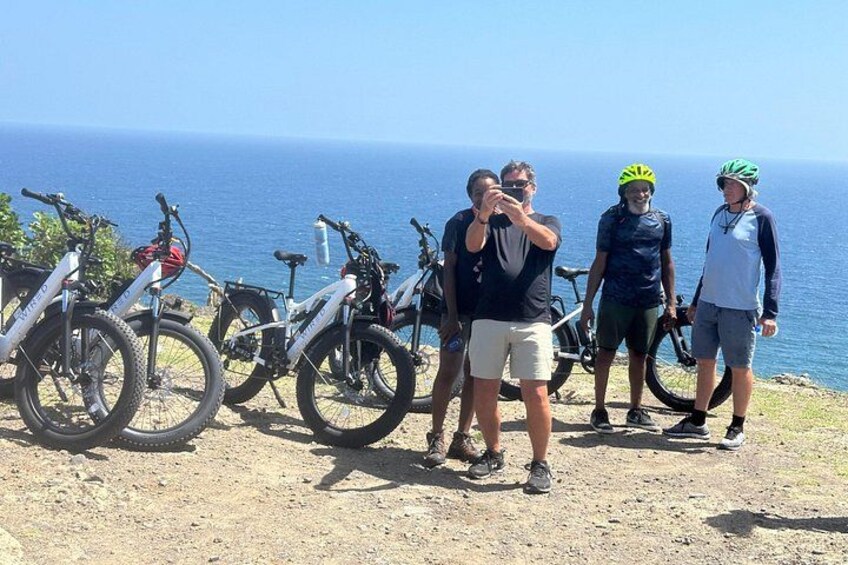 A group of people standing by a coastal road with bicycles parked nearby. 5