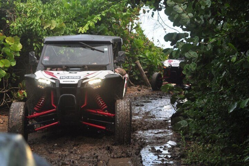 A white and red off-road vehicle navigating a muddy trail in a forested area. 1
