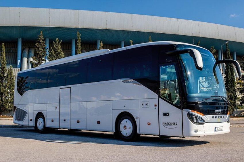 Een grote witte bus met 'SETRA'-reclame geparkeerd voor een modern gebouw met een blauw dak. 2