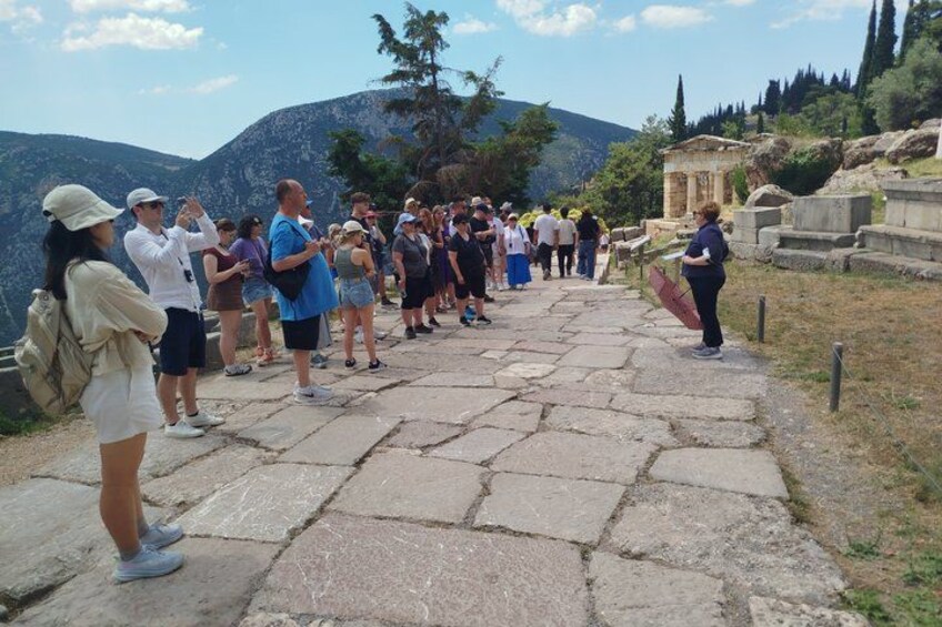 Een groep toeristen staat op een pad van stenen bij een archeologische plek, met ruïnes en bergen op de achtergrond. 5