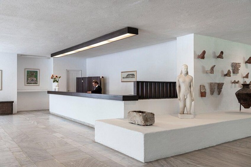 A modern reception area with a white counter, a bust sculpture, and various artifacts on the wall. 2