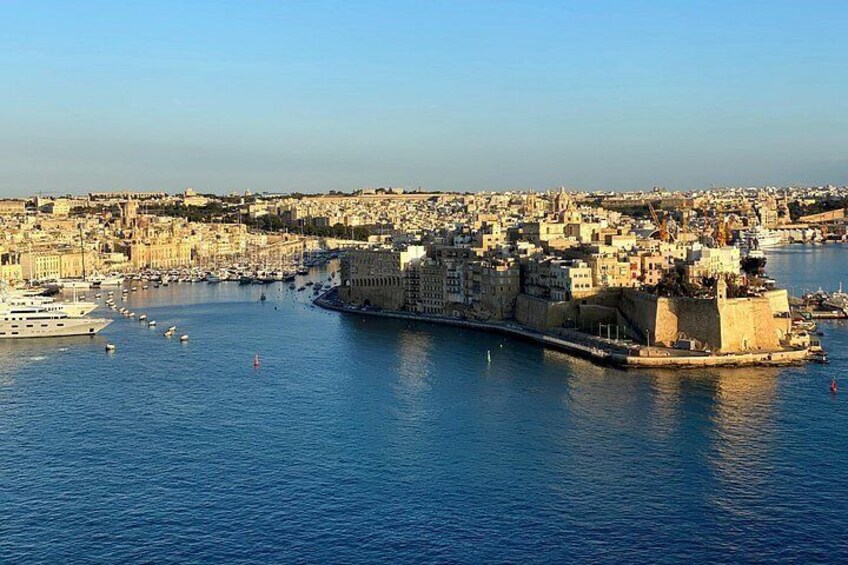 A coastal cityscape with a prominent fortified structure, a harbor with boats, and a densely built urban area. 2