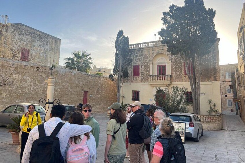 Un grupo de personas reunidas en una calle histórica con edificios de piedra y un árbol. 4