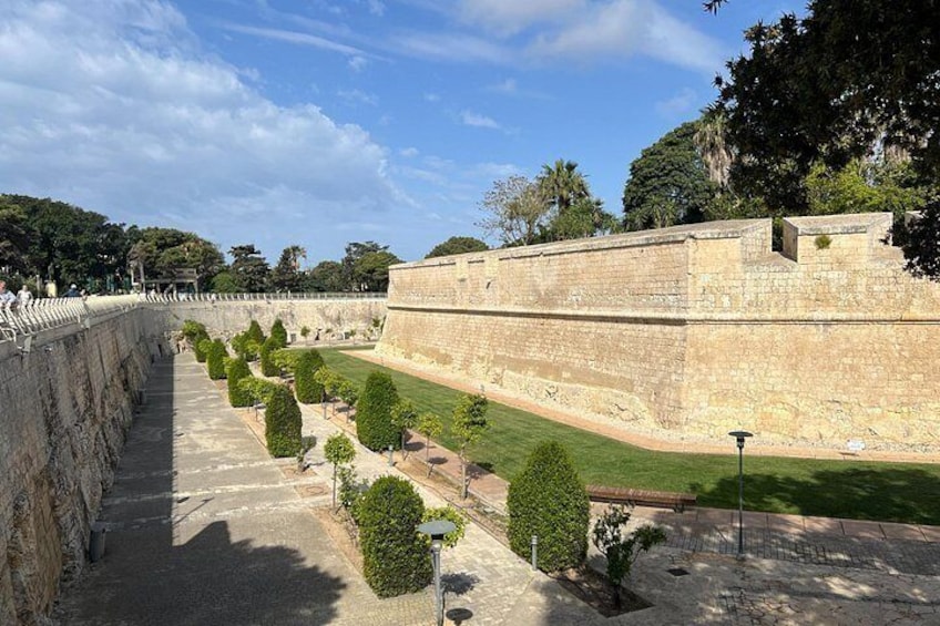 A stone fortification with a paved walkway and trimmed hedges. 2