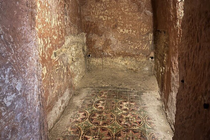 An ancient, dimly lit stone chamber with rough walls and a patterned floor. 5