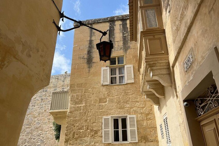 A narrow street with old buildings, a hanging lantern, and a window with shutters. 2