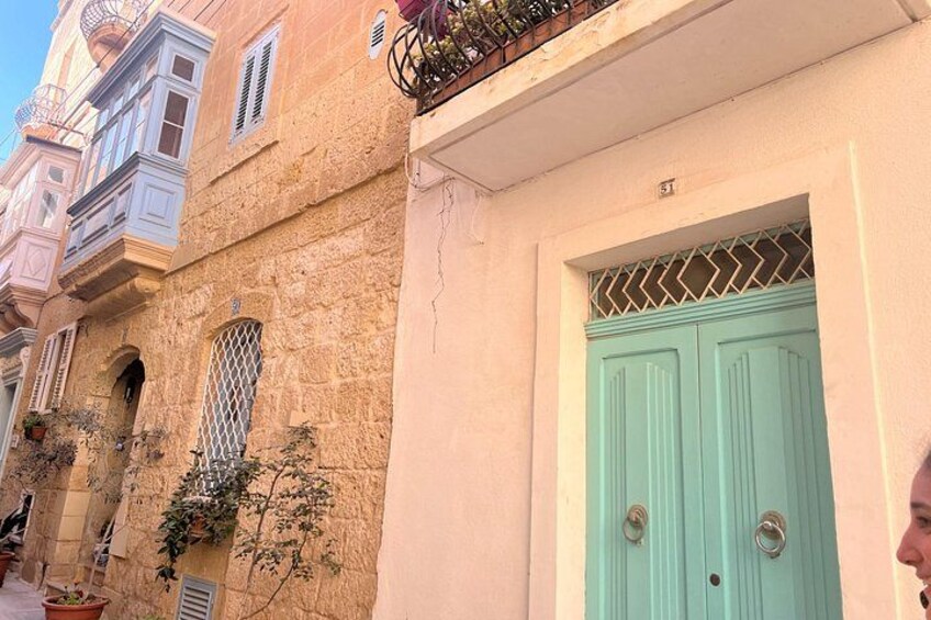A building with a green door, a window with a metal grille, and a balcony with plants. 3