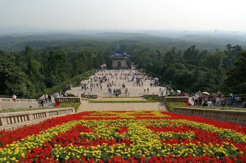A large open plaza with a central monument surrounded by colorful flower beds. 2