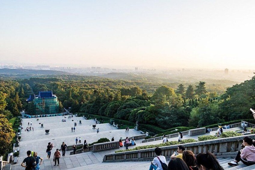 A park with a large open space, a building with a blue roof, and a densely wooded area. 1