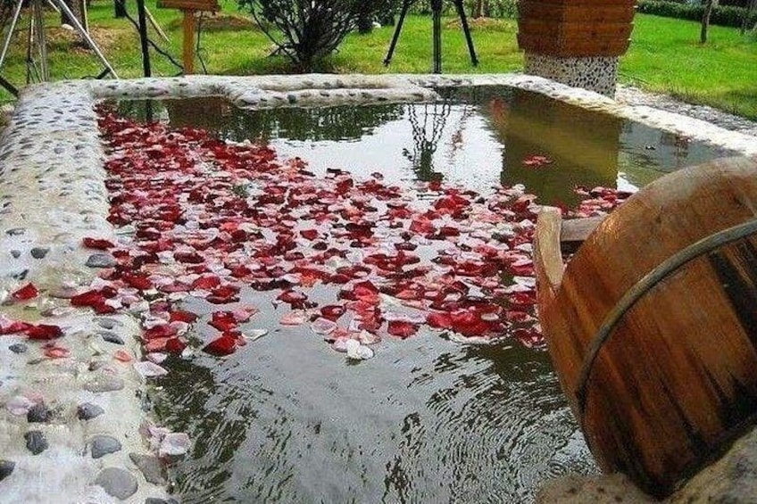 A pond with red flower petals floating on the water, surrounded by a stone border. 1