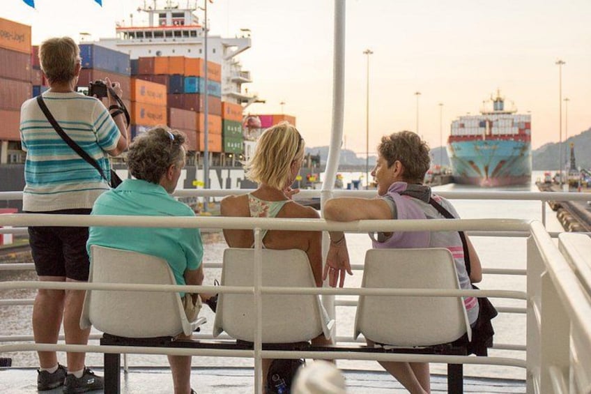 People sitting on a bench overlooking a port with cargo ships. 2
