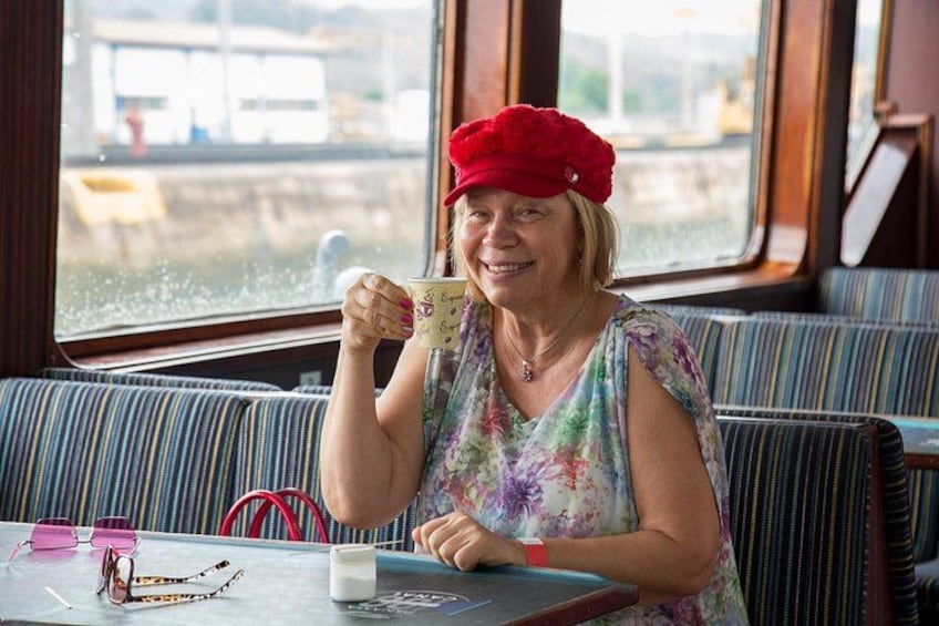 A person sitting at a table with a cup, wearing a red hat, and a floral dress. 3