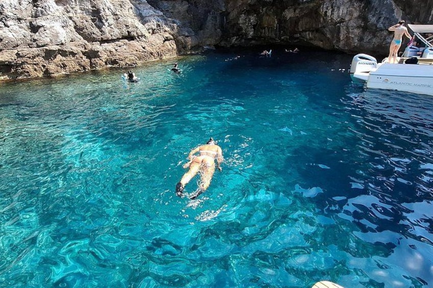 A person swimming in clear blue water near a rocky cliff and a boat. 5
