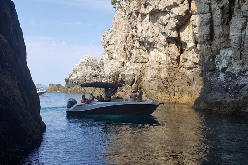 A boat anchored near rocky cliffs with clear water. 2