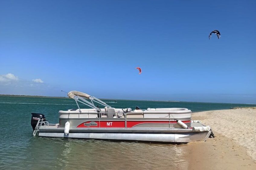 A boat on a sandy beach with a clear blue sky and a person flying a kite in the distance. 3