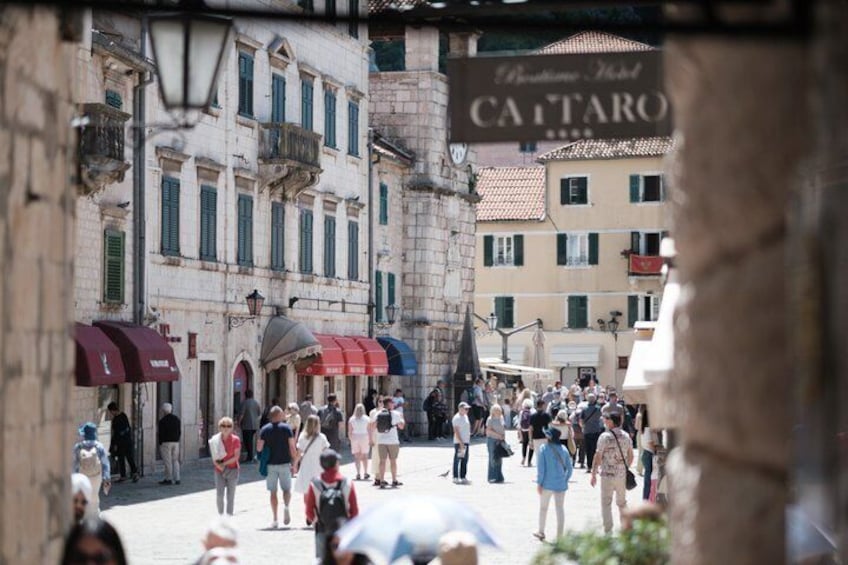 Une place animée, bordée de bâtiments historiques, un panneau indiquant « Cattaro », et des gens qui se promènent. 3