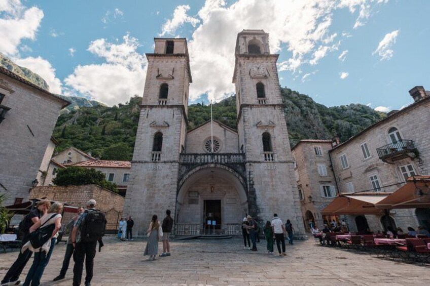 Une église historique en pierre, dotée de deux tours de clocher, une place pavée et des bâtiments environnants. 5