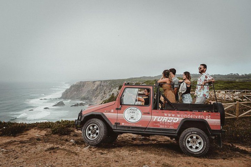 A red van with passengers on a coastal road. 4