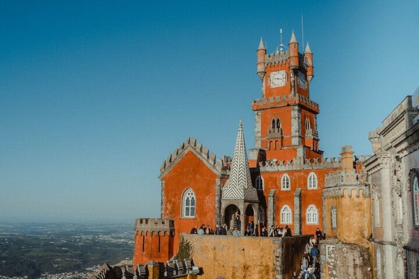 A castle with a clock tower, a pointed spire, and a view of the landscape. 2
