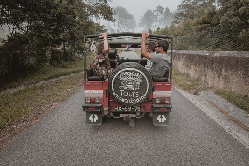 A red off-road vehicle with two passengers, a man and a woman, driving on a paved road surrounded by greenery. 2