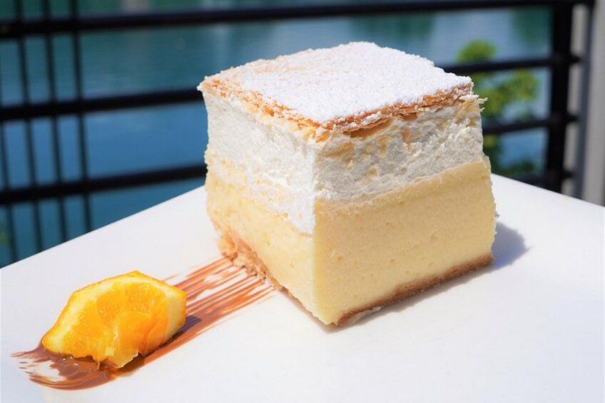 A slice of layered cake with a dusting of powdered sugar on top, placed on a white plate with a slice of orange on the side. 2