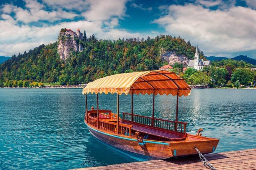 A wooden boat with a yellow canopy docked at a pier, a church, and a rocky mountain in the background. 5