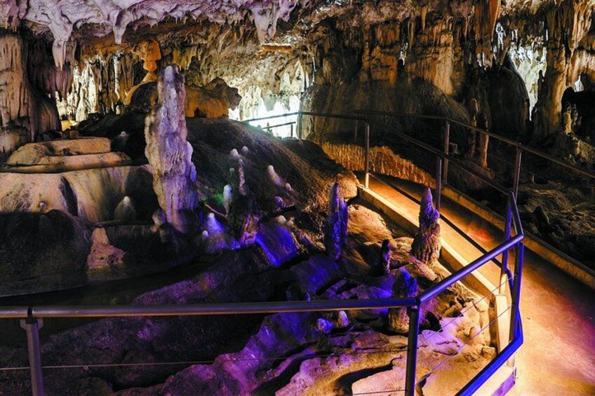 A cave with stalactites and stalagmites, a metal railing, and a staircase. 4