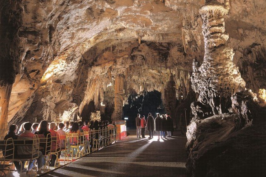 A cave with stalactites and stalagmites, a paved walkway, and visitors. 2
