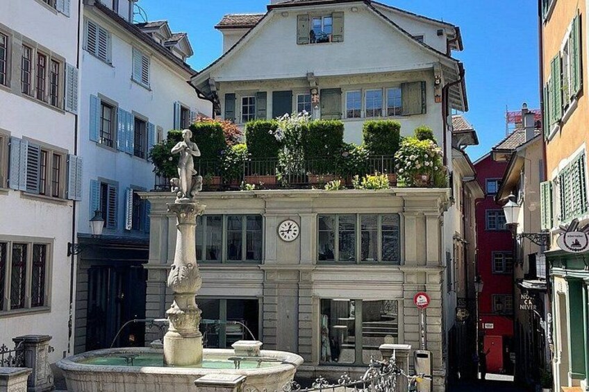 Un edificio histórico con una fuente, balcones con plantas y un reloj. 2