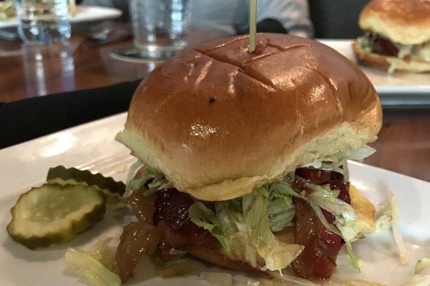 A burger with a bun, lettuce, and pickles on a white plate. 2