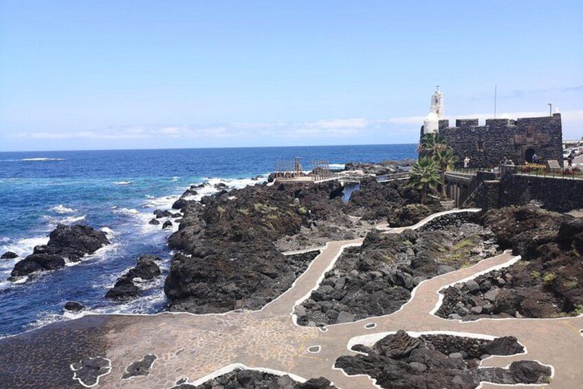 Paesaggio costiero con terreno roccioso, un faro e una struttura fortificata. 2